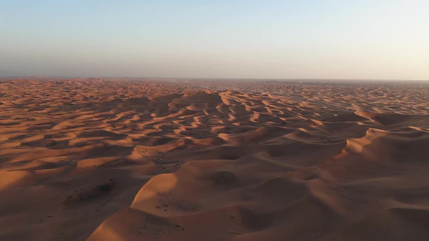 Sand dunes form an extensive desert landscape with trail marks on the surface