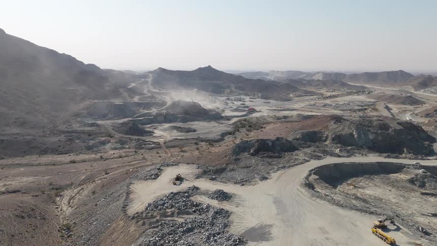 Heavy vehicles move on a work site near the mountains during the daytime
