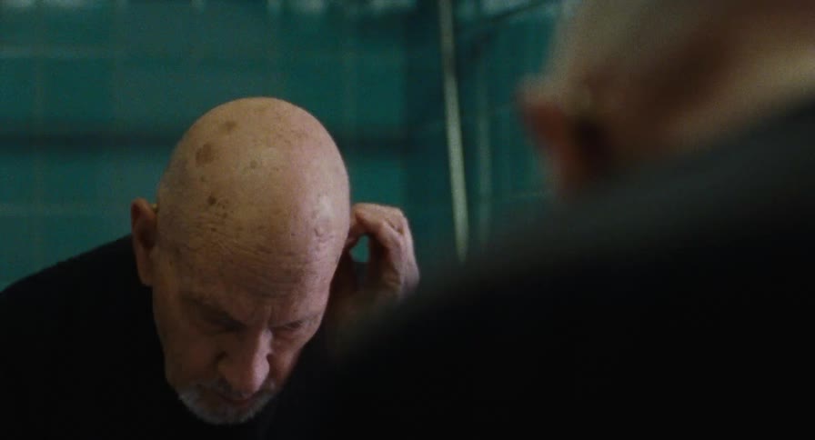 Old man puts in hearing aids in bathroom mirror