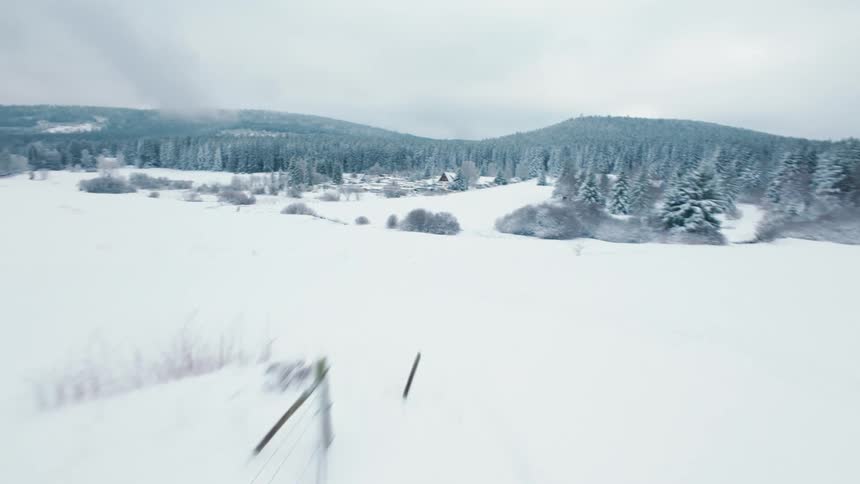 Snowcovered field with fences and houses in the distance surrounded by forest