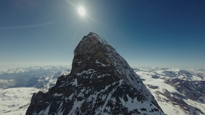 Snow on the rough terrain of a mountain peak as the sun shines brightly in the sky