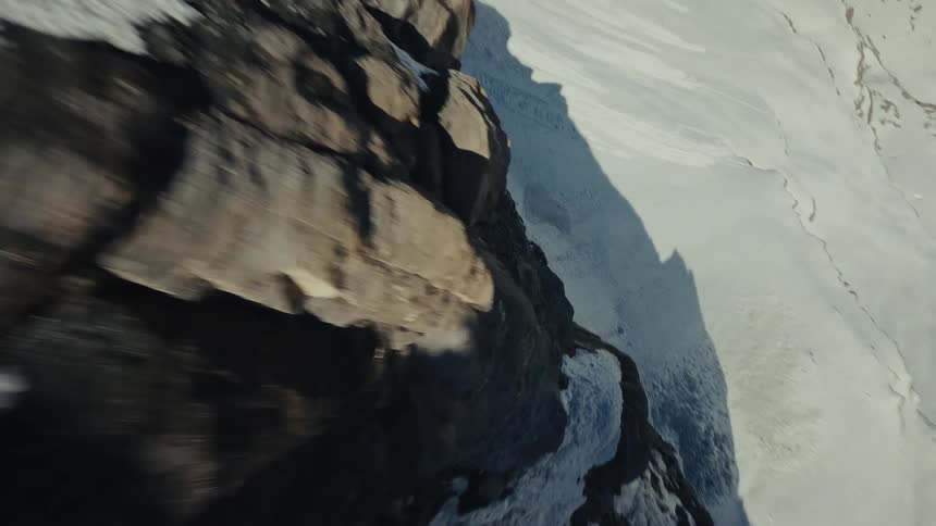 Snowcovered mountain slope with rock formations and peaks in the background