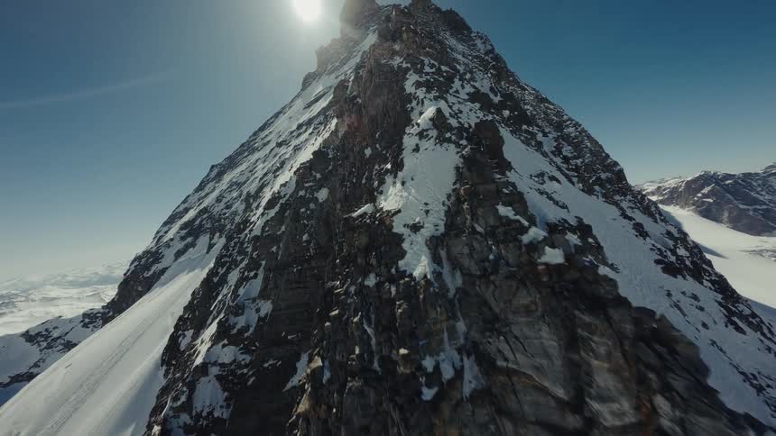 Moving over the rough terrain of a mountain ridge with snow covered mountains across the landscape