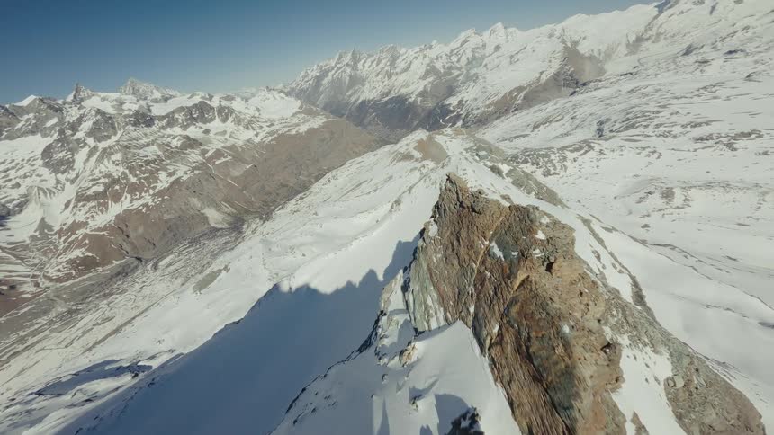 An aerial view of a mountain range covered in snow on a sunny day