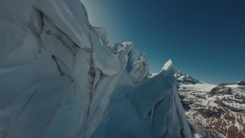 Glacier ice wall with deep crevasses beside snowcovered mountains