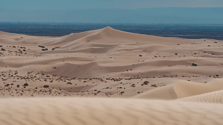 Rolling sand dunes stretch across a vast desert landscape under a clear blue sky