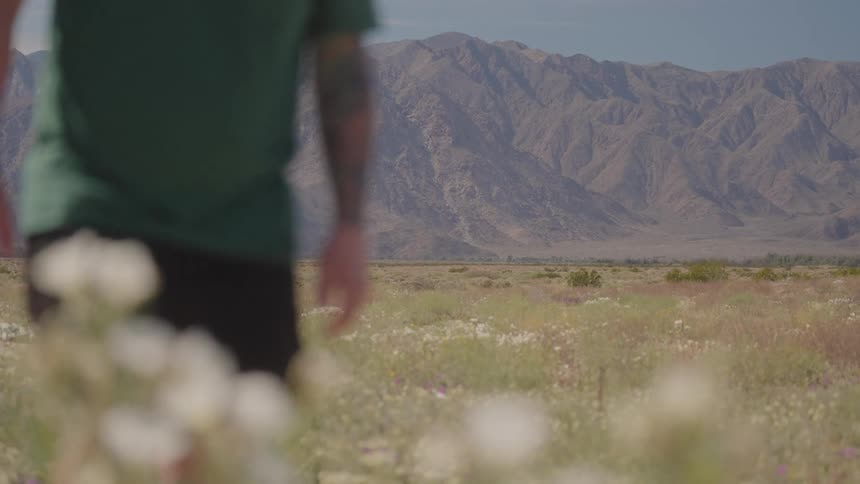 Blurred man walking through a flowered field in front of a dry mountain range