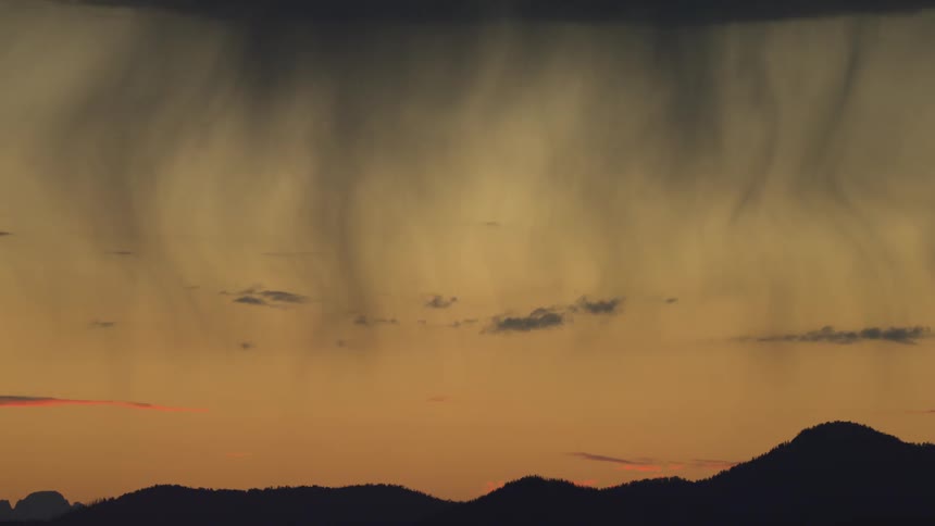 Dark clouds with rain curtains over mountains at sunset