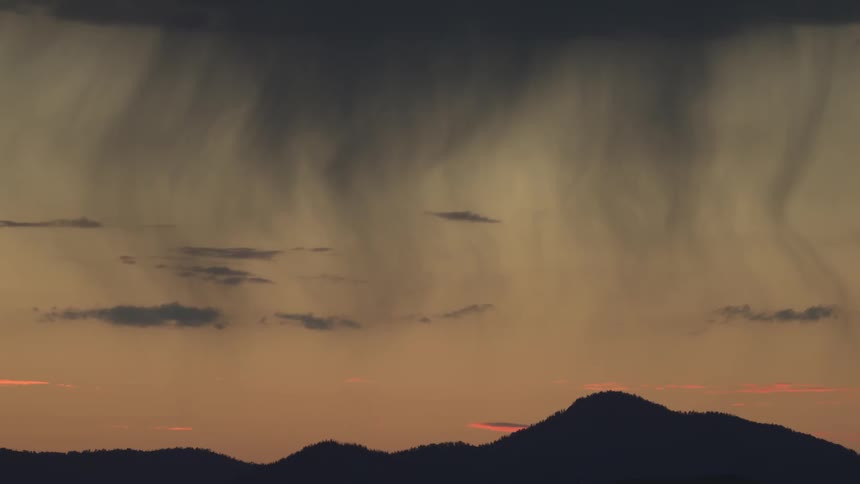 Rain shafts descending from clouds over mountain silhouettes at dusk