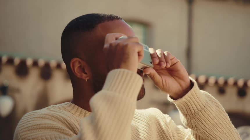 Person in light sweater uses camera in front of building with roof