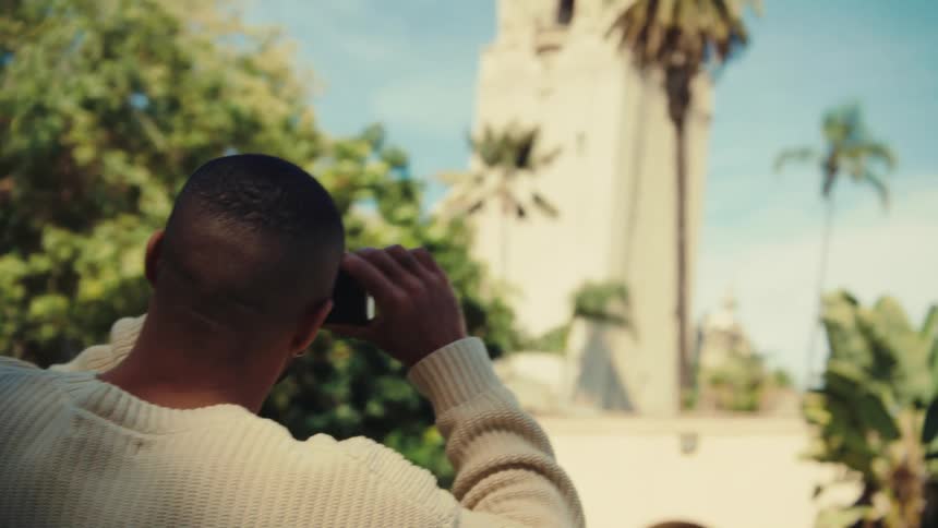 Man uses a phone to photograph a tower among palm trees outdoors