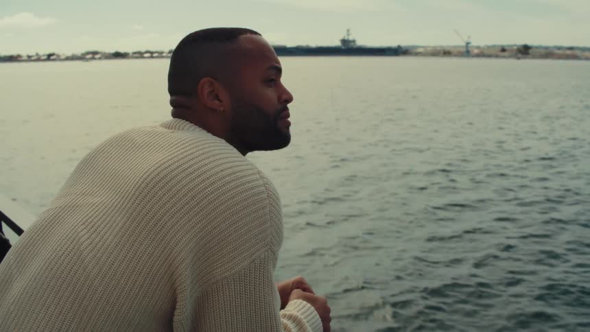 Man looks at the sea while leaning on a boat railing