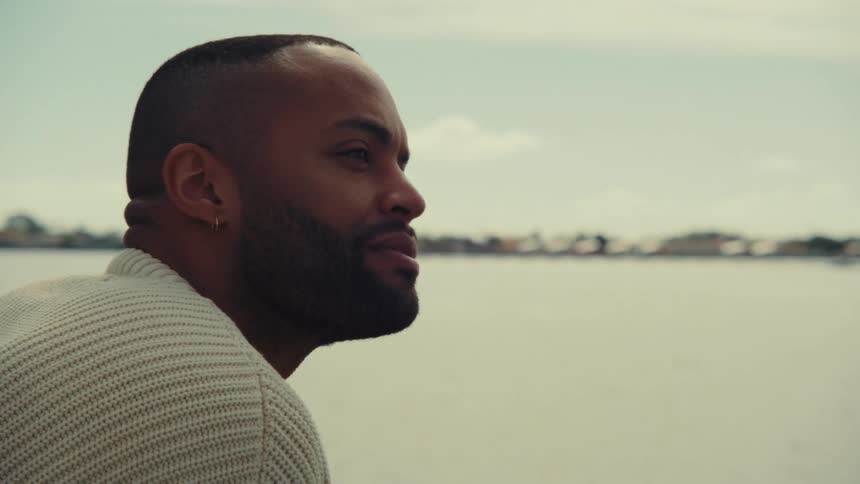 Bearded man looking toward the horizon by the water