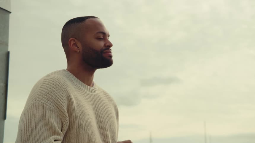 A smiling man relaxes while enjoying the outdoor view under a cloudy sky