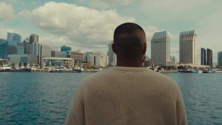 Man seen from behind observing an urban skyline across the water
