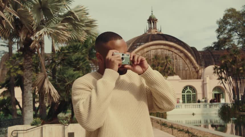 Person in light sweater photographs ornate building surrounded by palm trees