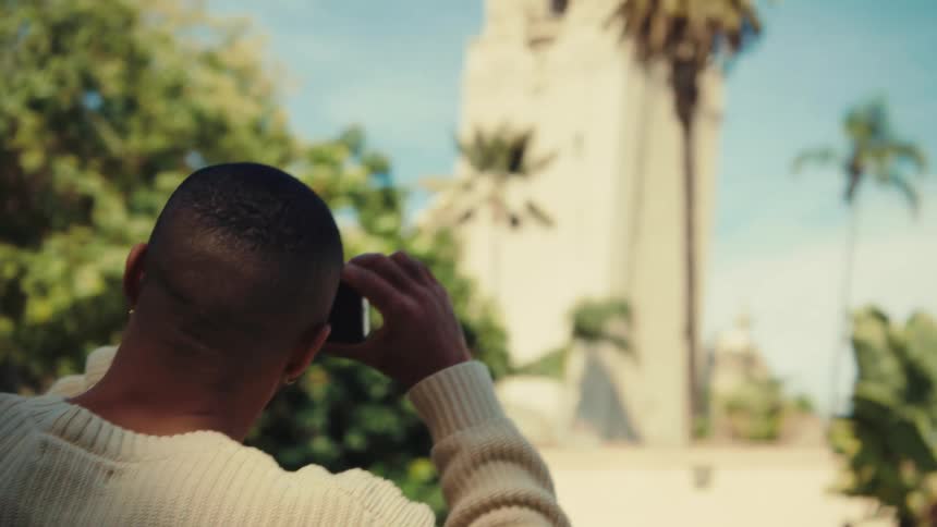 Person holding a phone while photographing a lightcolored tower surrounded by palm trees