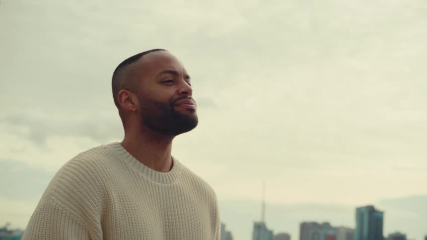 Person in light sweater holds cup in front of marina with buildings in background