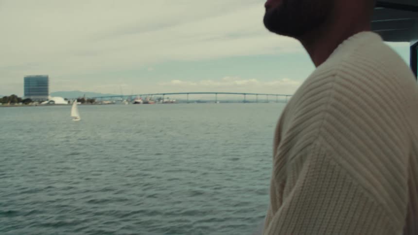 Man looks at the sea near a metal structure with a bridge in the background
