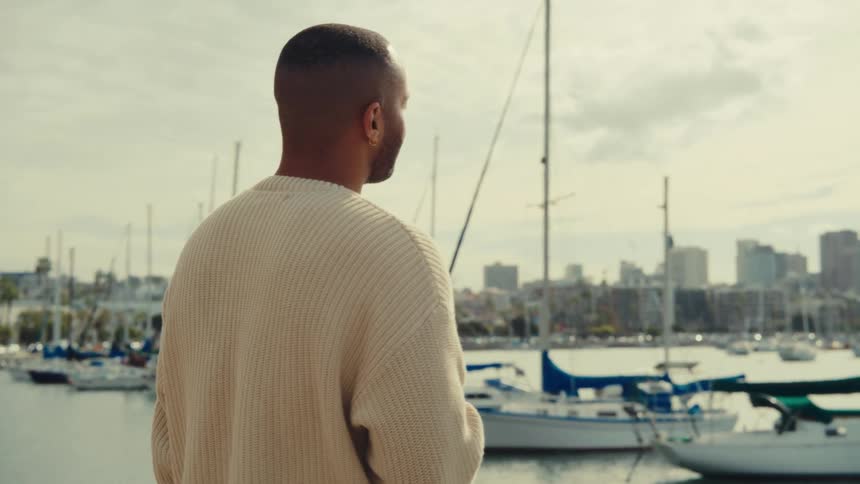 Man holds a cup as he walks along the coast overlooking the harbor
