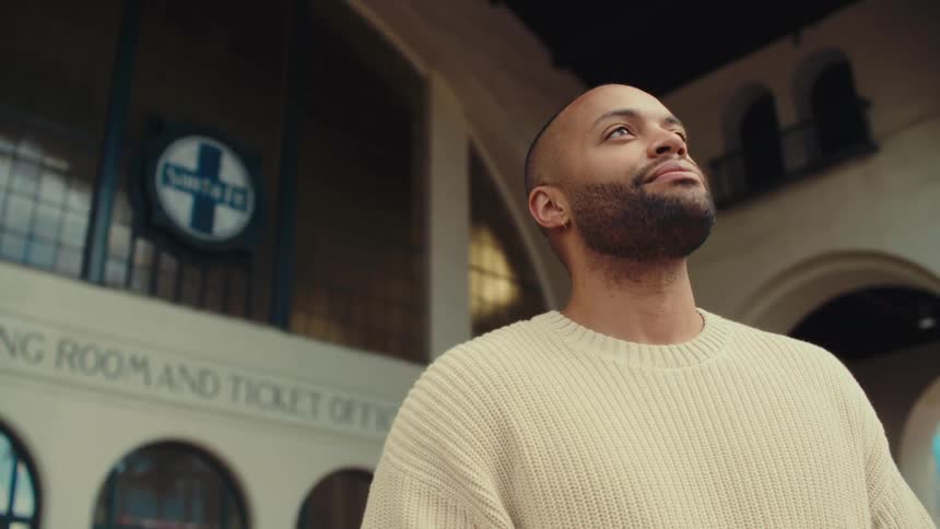 Bearded man looking upward in front of a building with arches