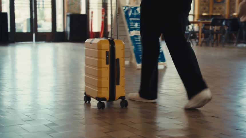 Yellow wheeled suitcase stands on the floor while a person stands beside it near the door