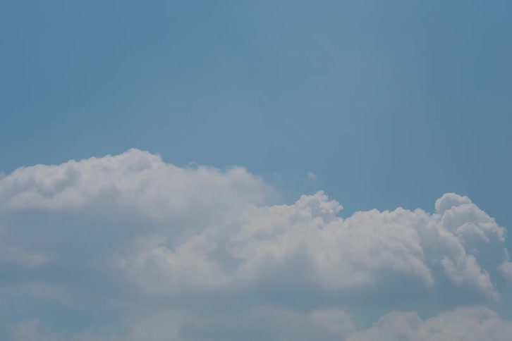 A time lapse view shows fluffy white clouds moving across a bright blue sky on a clear day with the sunlight illuminating the soft textures of the cloud formations