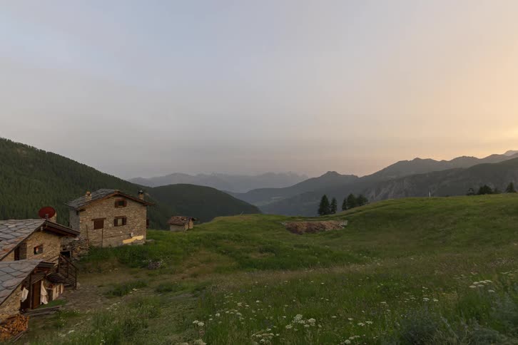 Man carrying a bag walks into a rural house in the mountains with mountains across the landscape