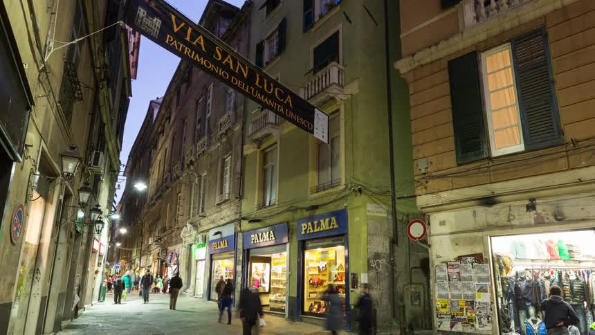 Narrow street lit at dusk with pedestrians shops and a via san luca sign between historic buildings