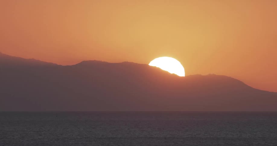 Sun rises over mountains in an orange sky