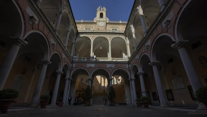 A symmetrical wide view of tourists exploring a grand courtyard with ornate arches and a central clock tower