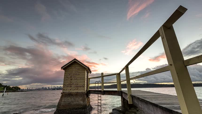 Two people walk on a pier to a building at a lake