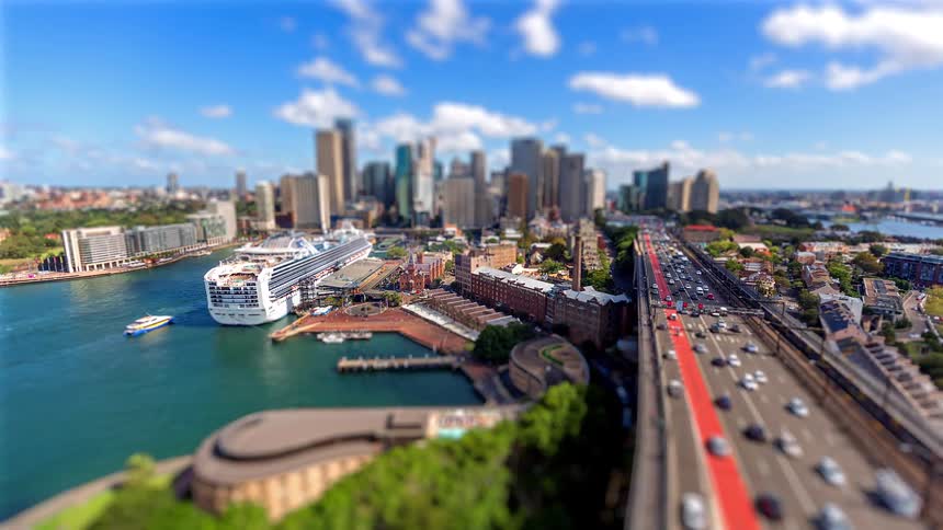 Traffic moves on a freeway into downtown with a cruise ship along the coast and a small boat sailing