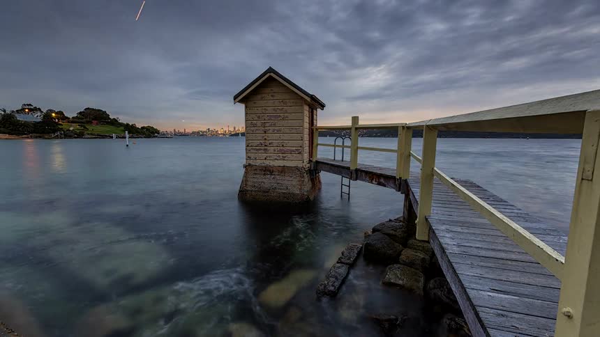 Small wooden structure over the water connected to a walkway under an evening sky