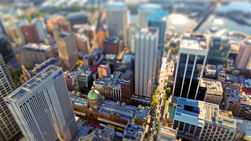 This tiltshift video provides a miniatureeffect aerial view of a bustling city center focusing on a historic building with a green domebusy streets and modern skyscrapers surround the heritage site with a bridge and waterfront visible