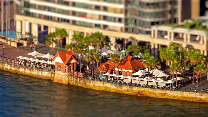 Restaurants with outdoor tables and umbrellas along a waterfront promenade with palm trees