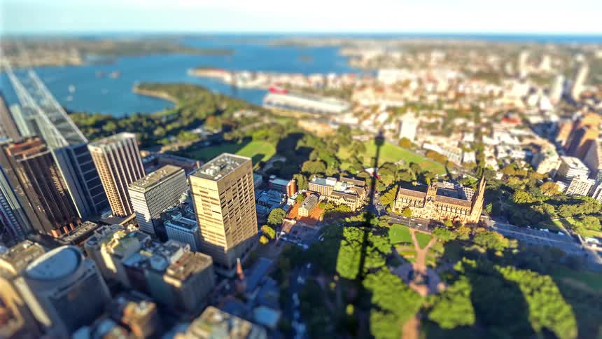 This video features a highangle tiltshift timelapse of sydney australia focusing on the area around hyde park and st marys cathedral a prominent shadow of the sydney tower stretches across the city landscape as the sun moves creating