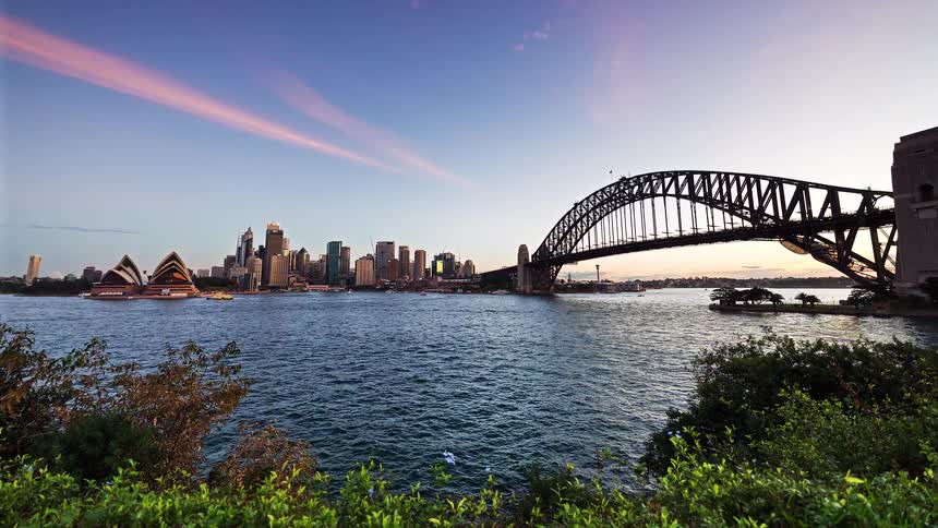 Illuminated bridge over the water with a city skyline and lit buildings at dusk