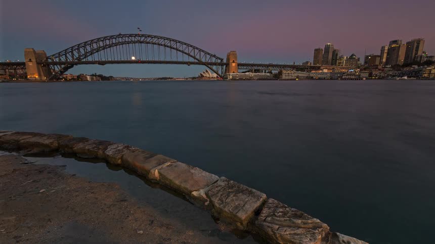 Watercraft move through the water of a night city as night falls