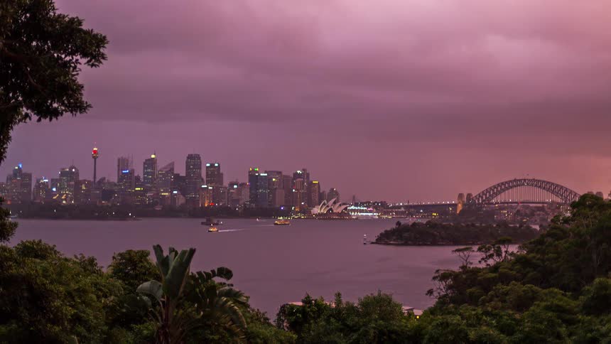 This timelapse captures the sydney skyline as the sky transitions from a fiery orange to a deep moody purple at duskthe iconic silhouettes of the sydney opera house and harbour bridge stand out against the city lights while boats move ac