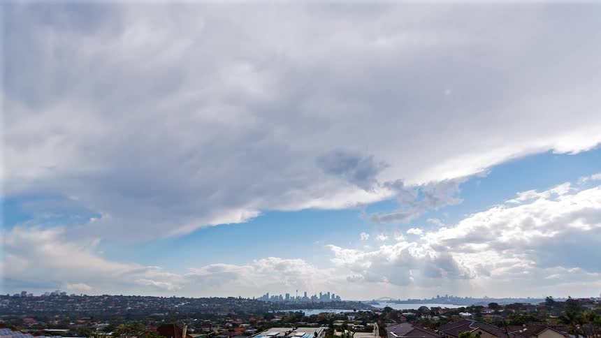 Residential neighborhood in the foreground with city and bay in the distance under dense clouds