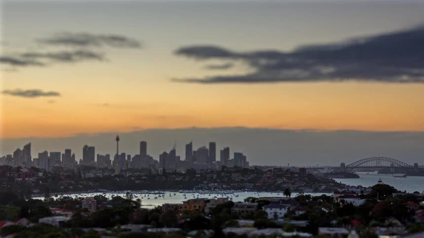 City skyline illuminated at dusk with tall buildings and a bridge over the bay in the background