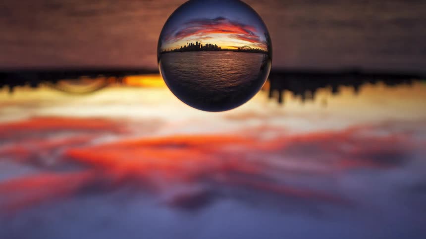 Glass sphere reflecting urban skyline and water at sunset
