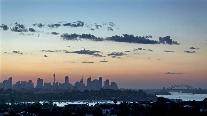 Sun sets over metropolitan buildings and skyscrapers on the sydney australia skyline on the coast as lights come on and traffic moves as night falls