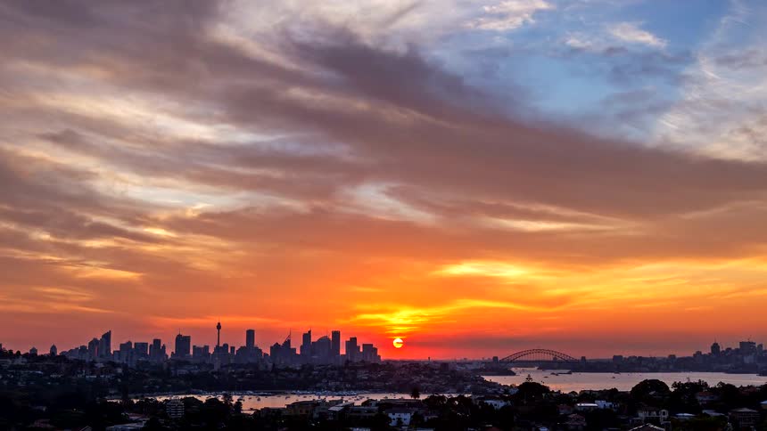 Sun setting behind the urban skyline with bay and bridge in the background