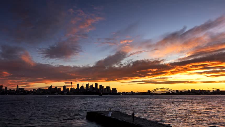 Urban skyline and bridge over a bay under a colorful sunset sky