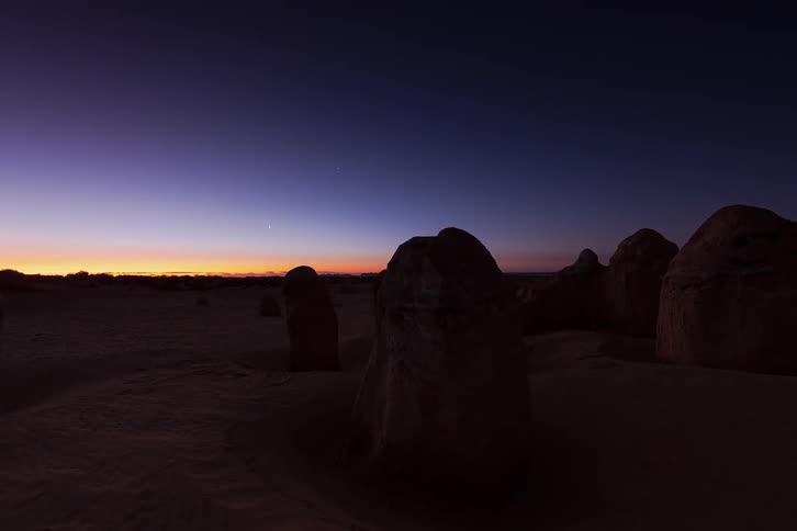 Boulders standing across the desert under a starry sky at dusk