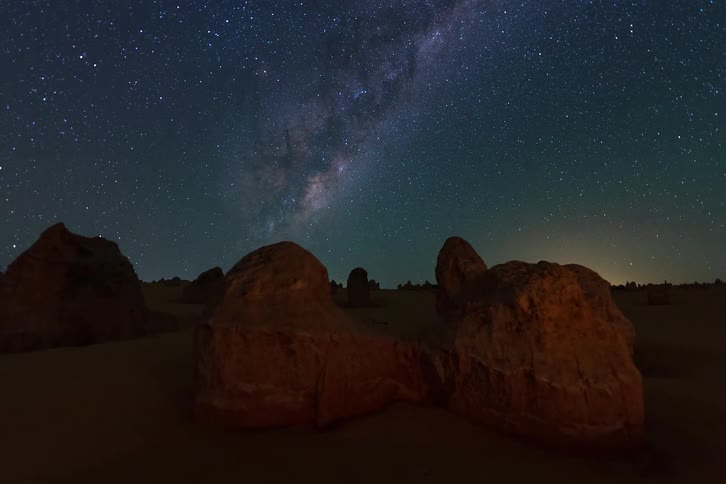 Milky way galaxy and stars shining above a desert landscape with rock formations at night