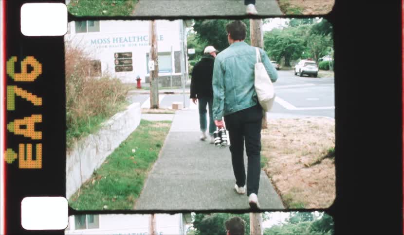Two people walk down a sidewalk past a health center one wearing a blue denim jacket and carrying a white tote bag
