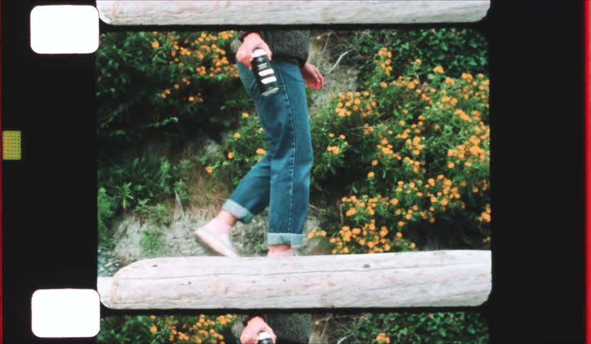 A woman wearing blue jeans and white sneakers walks across a large fallen log